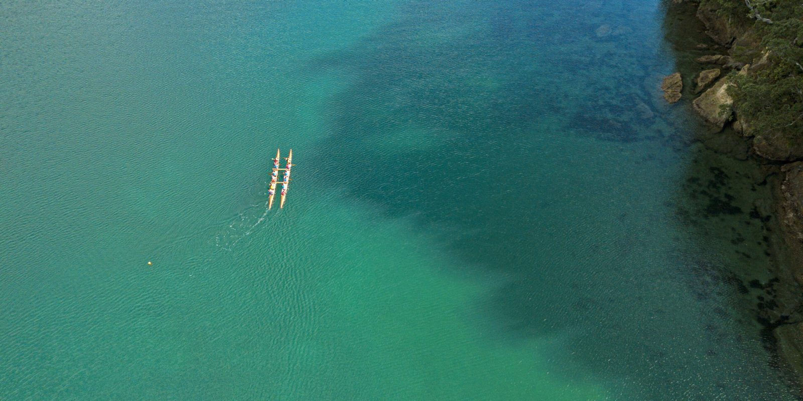 An aerial view captures the Waka ama 'Hukatai' as it is paddled across the serene waters of Aotea. Photo / Hillary Outdoors